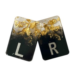 May include: Two rectangular resin pieces, one with the letter "L" and the other with "R", feature a black and white gradient design. Gold leaf flakes are embedded in the clear resin, adding a touch of luxury.