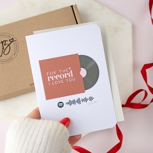 May include: A white greeting card featuring a vinyl record design and the text "FOR THE RECORD I LOVE YOU" on a terracotta-coloured square. A Spotify code is printed below. A brown box is in the background.