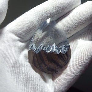 May include: A clear resin pendant with a mountain range design inside. The resin is clear and the mountains are a dark gray color. The pendant is shaped like a teardrop and is about 2 inches long.