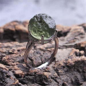 May include: A silver ring with a large, green, rough-cut gemstone set in a claw setting.