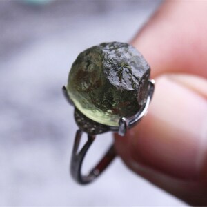 May include: A silver ring with a large, green, faceted gemstone. The gemstone is set in a silver bezel and the ring has a simple band.