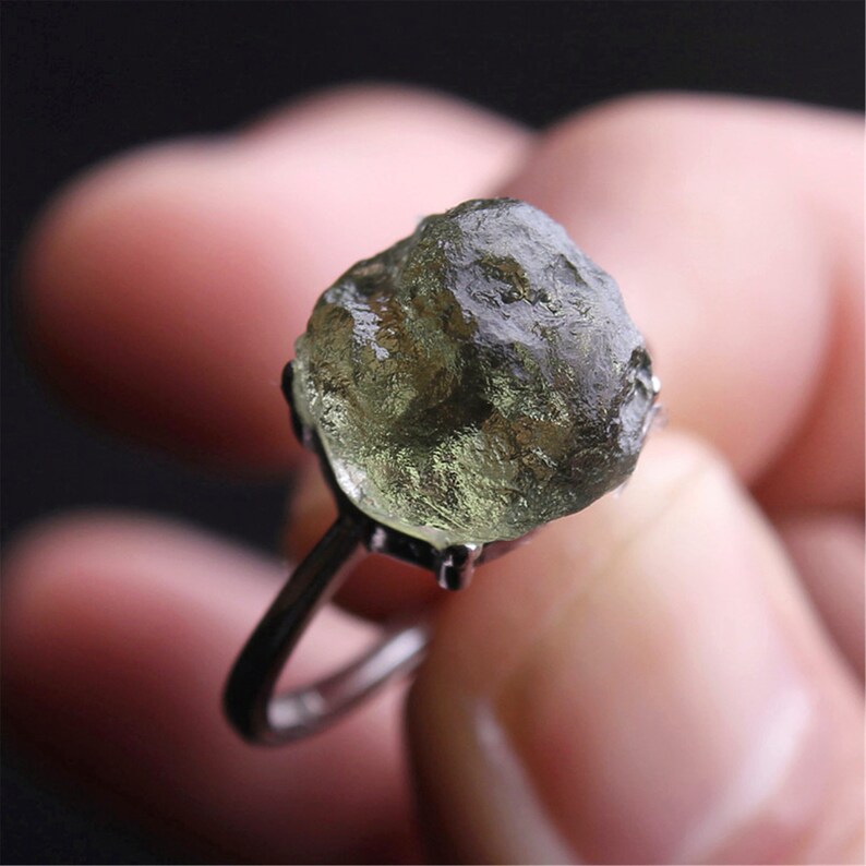 May include: A silver ring with a large, green, rough-cut gemstone. The gemstone is set in a prong setting.