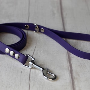 May include: A purple dog lead with a silver clip and silver accents. The lead is made of a durable, rubber-like material.
