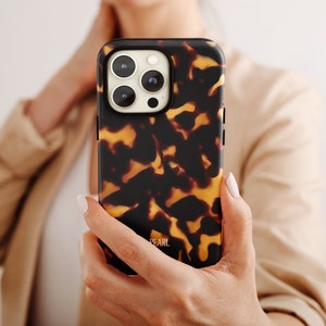 Może przedstawiać: Brązowe i czarne etui na telefon w stylu żółwim pancerzem z wycięciem na obiektyw aparatu i napisem "PEARL" na dole.