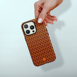 Può includere: Una custodia per telefono nera con un motivo geometrico rosso e arancione. La custodia ha un ritaglio per l'obiettivo della fotocamera e un piccolo logo in basso.