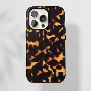Może przedstawiać: Czarne etui na telefon z wzorem imitującym pancerz żółwia. Etui ma wystający element na aparat i czarny przycisk z boku.