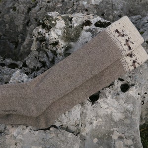 Puede incluir: Un par de calcetines de lana marr&oacute;n hasta la rodilla con un pu&ntilde;o blanco con un patr&oacute;n de renos. Los calcetines est&aacute;n doblados y colocados sobre una roca gris.