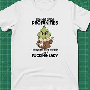 May include: White t-shirt with a graphic of a green cartoon character holding a coffee cup and giving the middle finger. The text reads "I DO NOT SPEW PROFANITIES, I ENUNCIATE THEM CLEARLY LIKE A FUCKING LADY."