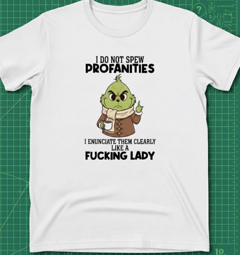 May include: White t-shirt with a graphic of a green cartoon character holding a coffee cup and giving the middle finger. The text reads "I DO NOT SPEW PROFANITIES, I ENUNCIATE THEM CLEARLY LIKE A FUCKING LADY."