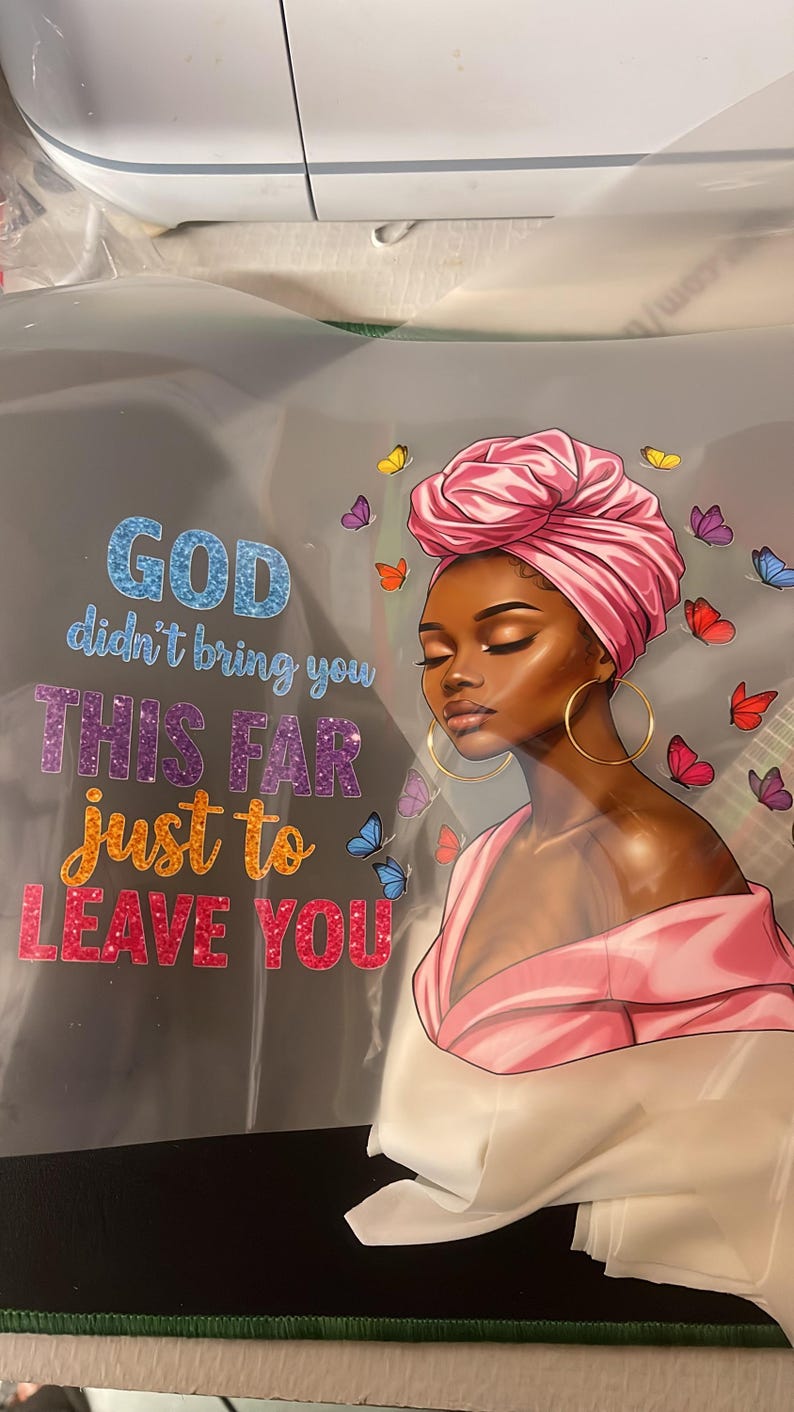 May include: Illustration of a woman with a pink head wrap and gold hoop earrings, surrounded by colorful butterflies. Text reads "GOD didn't bring you THIS FAR just to LEAVE YOU" in glittery letters.