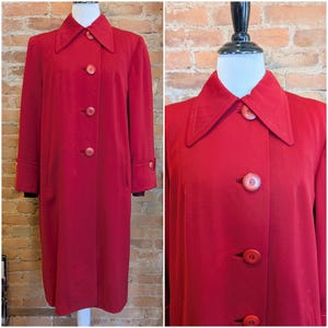 May include: A long-sleeved, knee-length red coat featuring a pointed collar, a front button closure with four visible round red buttons, and buttoned cuffs. The garment has a structured silhouette with clean lines and a solid, uniform red color.