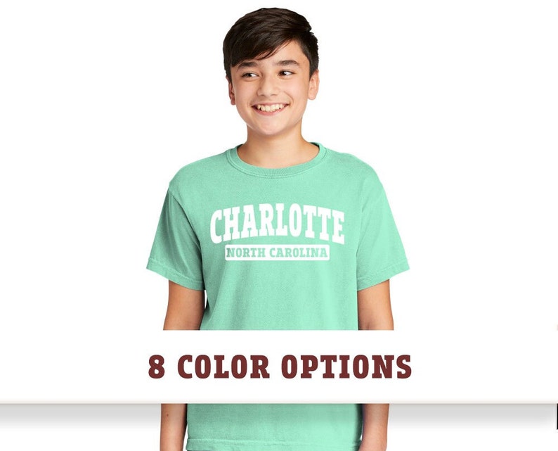 May include: A light green t-shirt with a white graphic that says "CHARLOTTE NORTH CAROLINA" in a vintage collegiate style font.