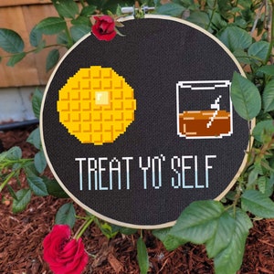 May include: A black embroidery hoop with a yellow waffle, a glass of brown liquid, and the text "TREAT YO' SELF" in white.