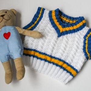 Puede incluir: Chaleco sin mangas de punto blanco con rayas azules y amarillas. El chaleco tiene cuello en V y está hecho de un hilo suave y texturizado.