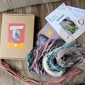 May include: DIY plant hanger kit with instructions, a wooden ring, and four skeins of yarn in pink, gray, blue, and beige.
