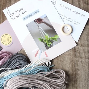 May include: DIY plant hanger kit with instructions, a wooden ring, and four spools of macrame cord in pink, gray, white, and blue.