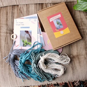 May include: DIY macrame plant hanger kit with instructions, three skeins of yarn in shades of blue and white, and a wooden ring. The kit includes instructions for creating a spiral knot macrame plant hanger.