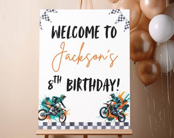 May include: A white sign on an easel with the text "WELCOME TO Jackson's 8th BIRTHDAY!" in black and orange. The sign features illustrations of motocross riders and checkered flags, with balloons in the background.