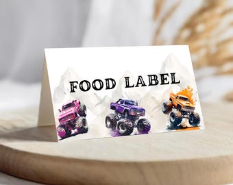 May include: A white folded card with the text "FOOD LABEL" in black. The card features watercolour illustrations of three monster trucks in pink, purple, and orange. The background shows a mountain range.