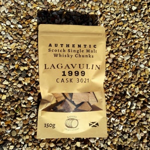 Op de afbeelding: Een bruine papieren zak met een label waarop staat "AUTHENTIC Scotch Single Malt Whisky Chunks", "LAGAVULIN 1999" en "CASK 3021". De zak bevat stukjes hout en heeft een label onderaan met de tekst "150g BARREL CRAFT STUDIO".