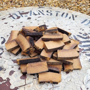 Op de afbeelding: Een stapel kleine, rechthoekige stukken eikenhout met verkoolden randen. Het hout heeft een lichtbruine kleur met zichtbare nerf. Deze stukken hout zijn waarschijnlijk bedoeld voor het roken of op smaak brengen van voedsel.