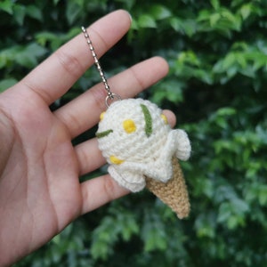 May include: A crocheted ice cream cone keychain with white and yellow yarn, green accents, and a silver chain.