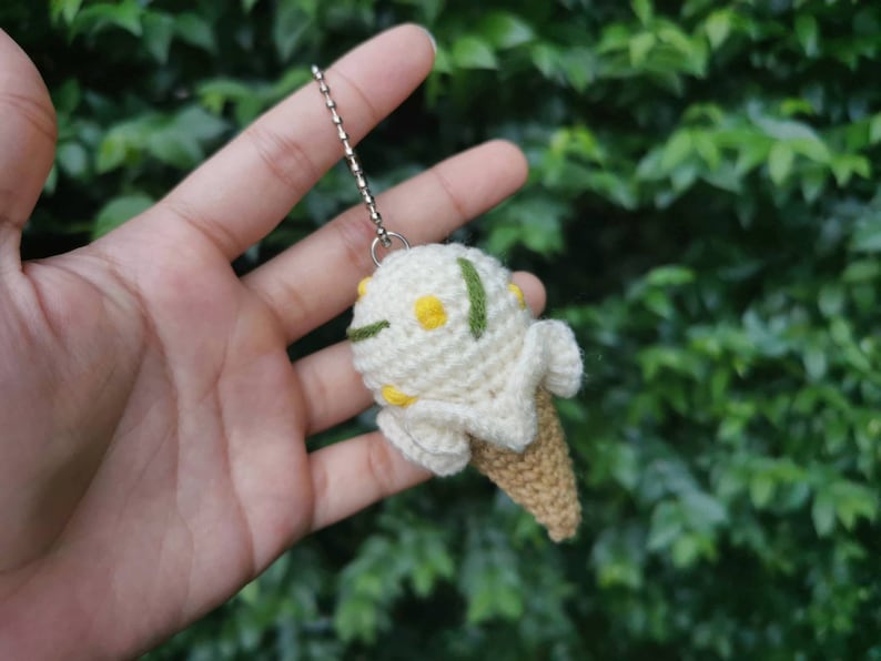 May include: A crocheted ice cream cone keychain with white and yellow yarn, green accents, and a silver chain.