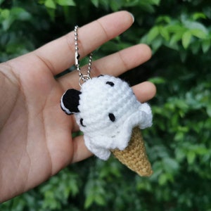 May include: A white crocheted ice cream cone keychain with black chocolate chips. The keychain is attached to a silver chain.