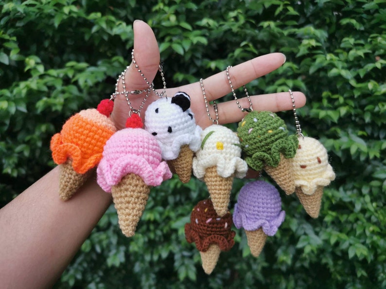 May include: A collection of eight crocheted ice cream cone keychains in various colors and flavors, including orange, pink, white, green, and purple.