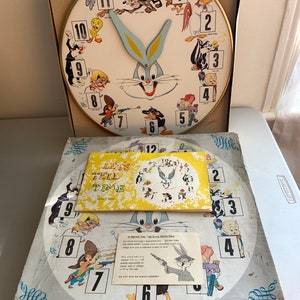 May include: Vintage Bugs Bunny electric clock featuring Bugs Bunny's face and other Looney Tunes characters around the clock face. The clock has a gold-colored rim and blue hands. The clock is in its original box with instructions.