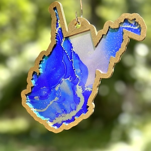 May include: Gold-colored West Virginia state outline ornament with a blue and gold marbled design inside.
