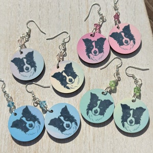 May include: Eight pairs of earrings featuring a black and white border collie dog on a round wooden disc. The earrings are available in a variety of colors, including pink, blue, green, and yellow.