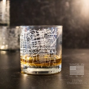 May include: A clear glass tumbler with an etched design of the San Francisco city map. The glass is filled with a brown liquid and the text "San Francisco" is visible on the glass. The text "Made in U.S.A. Urban Engravings" is visible below the glass.