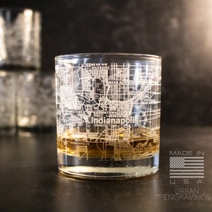 May include: A clear glass with an etched design of the Indianapolis city map. The glass is filled with a brown liquid and is sitting on a dark surface. The text "Indianapolis" is visible on the glass. The text "Made in U.S.A." and "Urban Engravings" is visible below the glass.