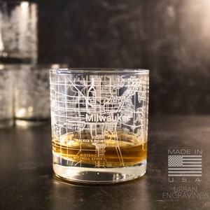 May include: A clear glass with an etched map of Milwaukee, Wisconsin. The glass is filled with a brown liquid and has the words "Milwaukee" and "Made in U.S.A. Urban Engravings" printed on it.