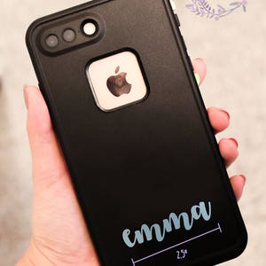 May include: Black phone case with a white apple logo and the name "emma" written in light blue cursive lettering. The case has a 2.5 inch measurement line below the name.