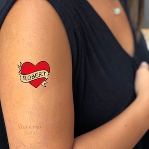May include: A red heart with a banner that says "ROBERT" in black lettering. The heart is outlined in black and has a white highlight. The banner is yellow with a black outline.