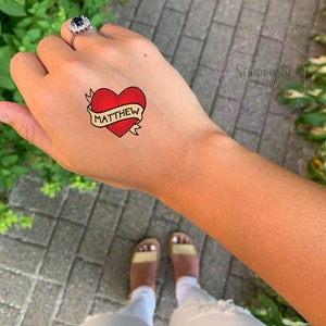 May include: A temporary tattoo with a red heart and a banner that says "MATTHEW".