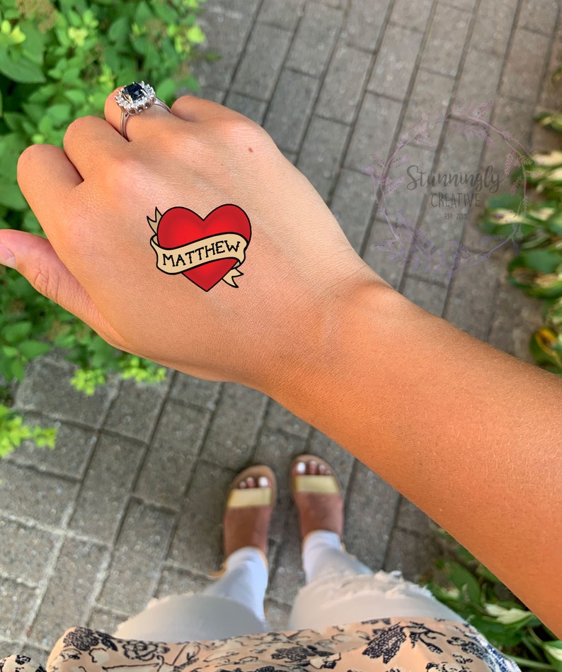 May include: A temporary tattoo with a red heart and a banner that says "MATTHEW".
