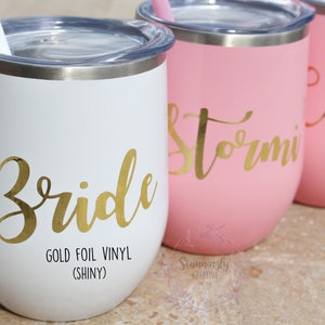 May include: Four stainless steel wine tumblers with gold foil vinyl lettering. The tumblers are white, pink, and pink. The lettering says "Bride", "Stormi", and "Carrie".