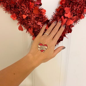 Puede incluir: Un tatuaje temporal con un coraz&oacute;n rojo y una pancarta que dice "Krista & Joseph".