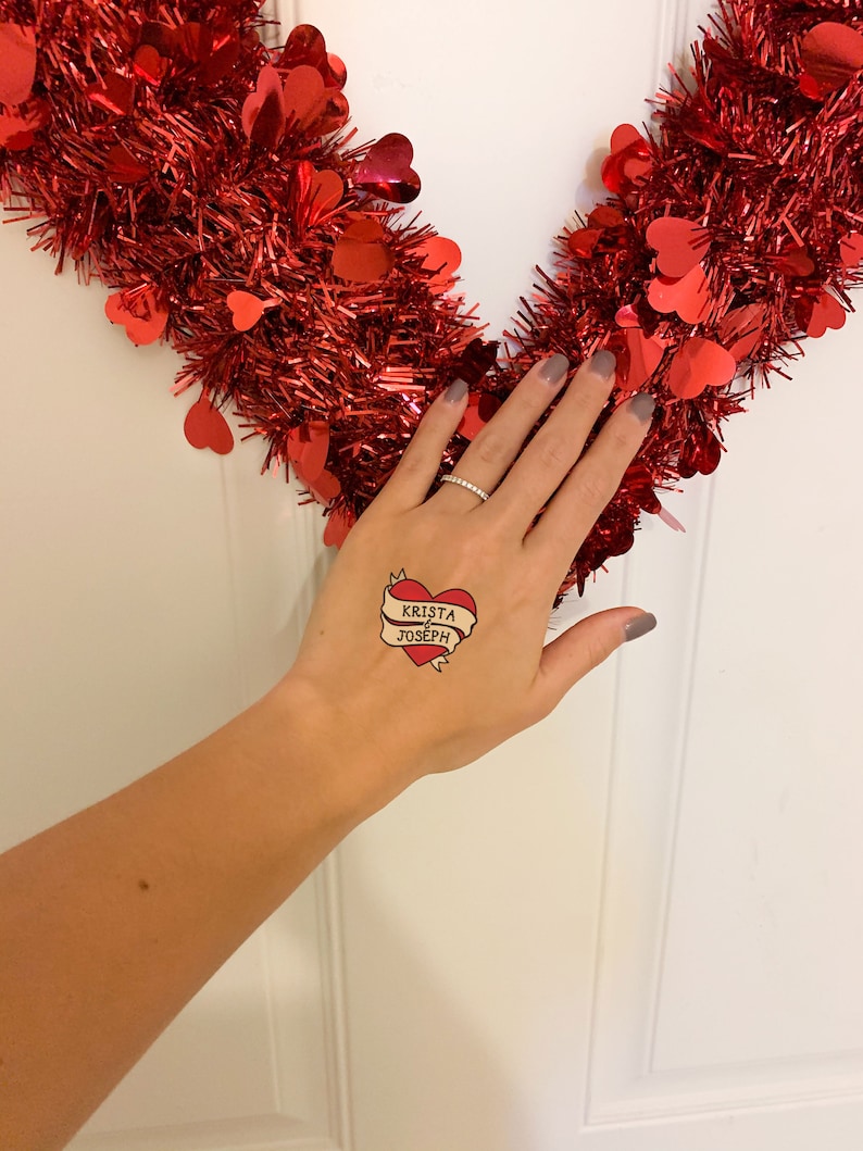 Puede incluir: Un tatuaje temporal con un coraz&oacute;n rojo y una pancarta que dice "Krista & Joseph".
