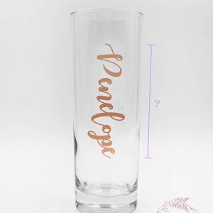 May include: A clear glass vase with a rose gold inscription that reads " Penelope" on the front. The vase is 5 inches tall.