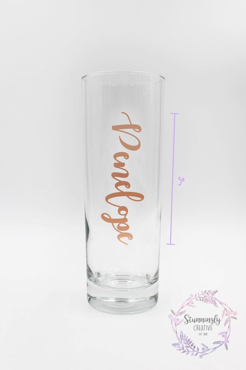 May include: A clear glass vase with a rose gold inscription that reads " Penelope" on the front. The vase is 5 inches tall.