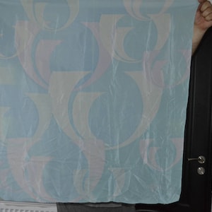 Puede incluir: Tela azul claro con un patrón repetitivo de formas abstractas en blanco, rosa y naranja claro. La tela se sostiene, mostrando toda su superficie. El material parece fino y posiblemente translúcido.