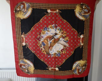 May include: A red, black, and gold patterned silk scarf with a design of two ducks in flight. The ducks are surrounded by floral and geometric patterns.