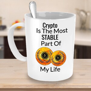 May include: White ceramic coffee mug with a black and yellow design. The mug reads "Crypto Is The Most STABLE Part Of My Life" with two yellow Bitcoin symbols.