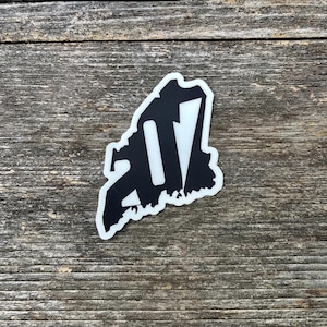 May include: A black and white sticker with the number 2017 in a distressed font. The sticker is on a wooden surface.