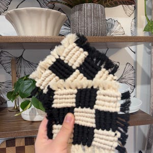 May include: Two black and white checkered macrame coasters with fringe. The coasters are handmade and have a modern farmhouse style.