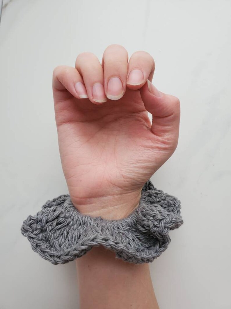 May include: A gray crocheted hair scrunchie with a ruffled edge.